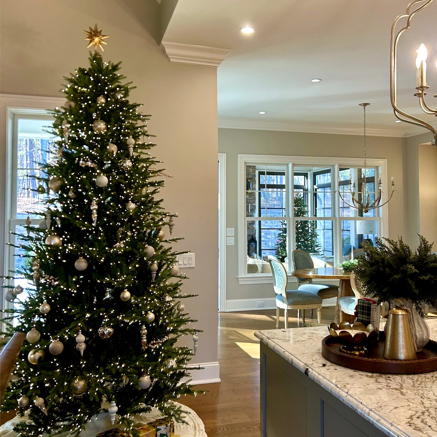 A tall Christmas tree with warm lights beside bright windows in a Triangle home