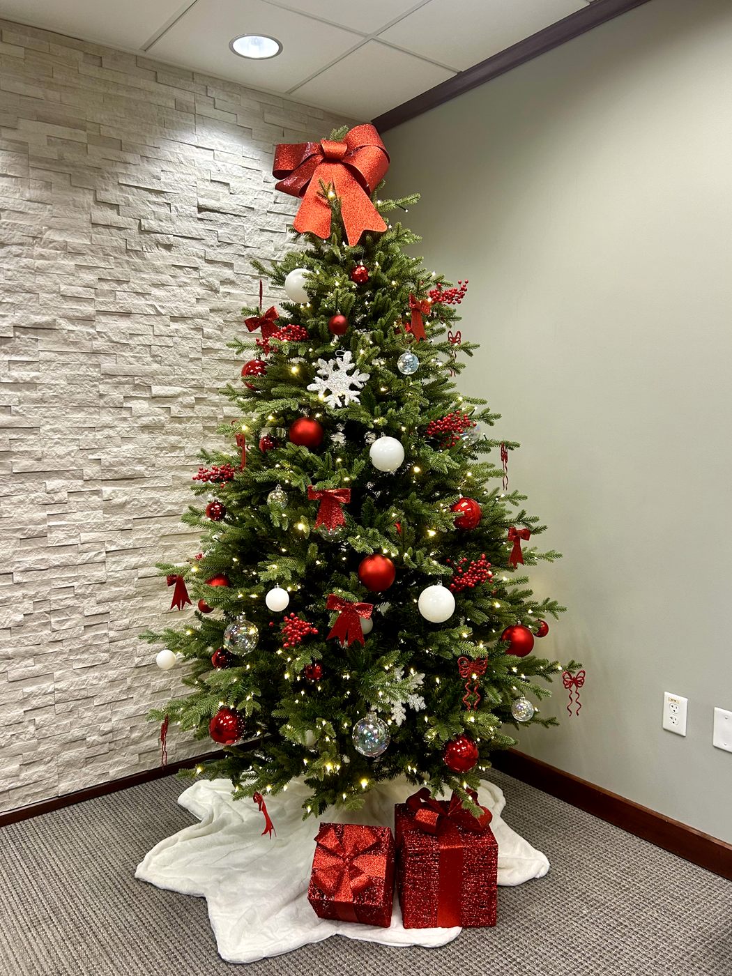 A red and white decorated Christmas tree with wrapped gifts in an office