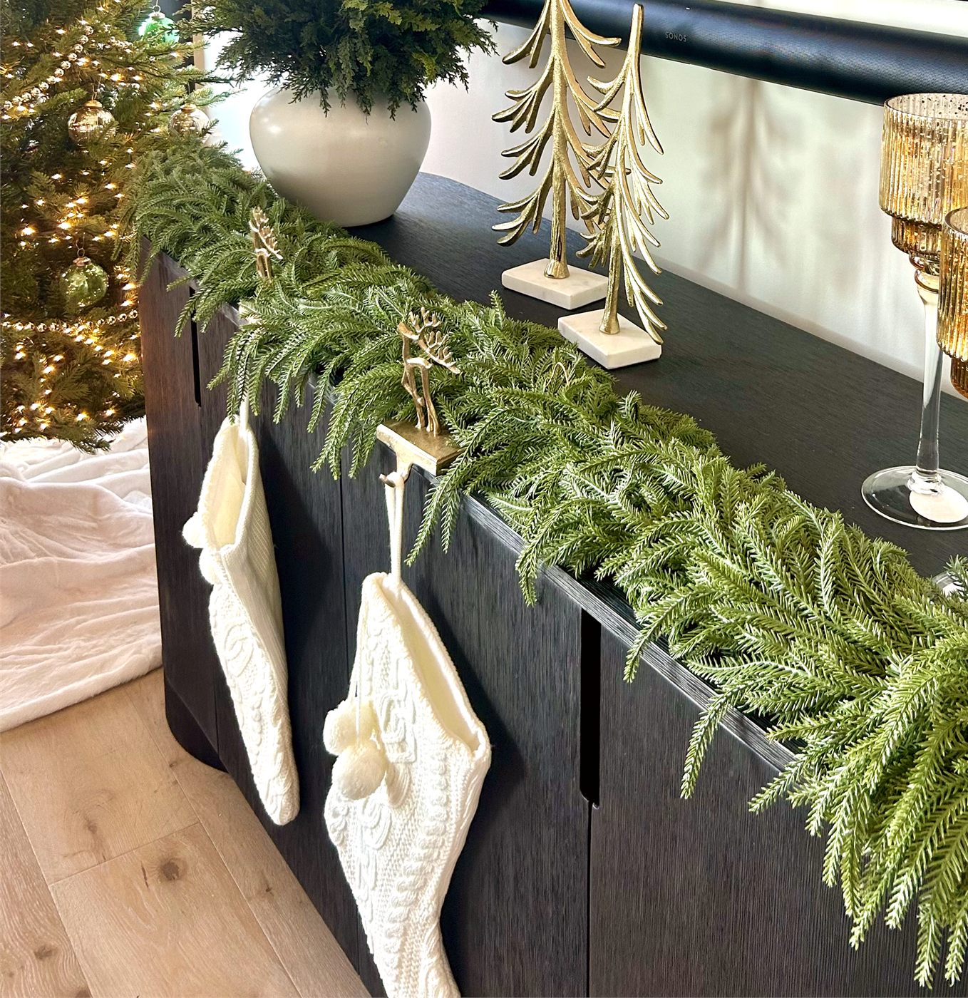 Fresh garland, gold candle holders, and white stockings styled along a console