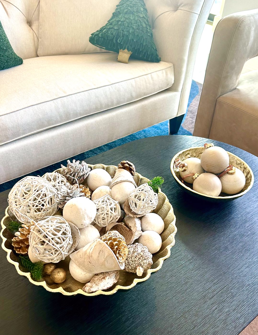 A bowl of white, gold, and natural ornaments on a coffee table beside a sofa