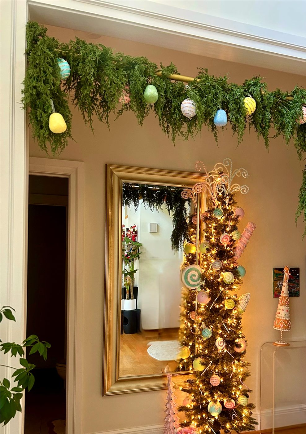 An entryway with a garland of pastel ornaments over the doorway and a slim decorated tree